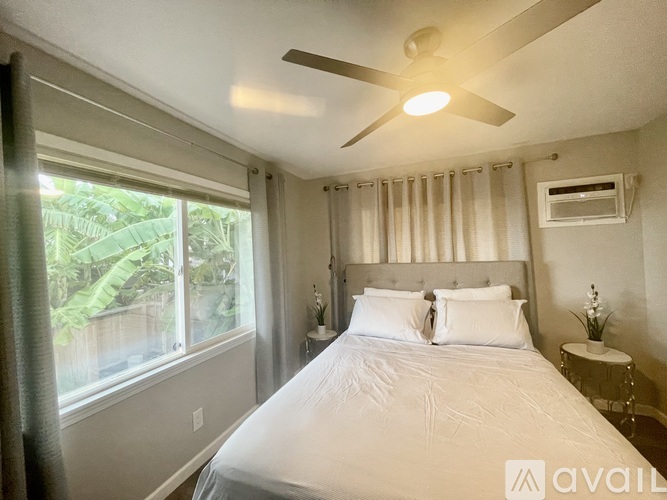 A bedroom with a large bed, a ceiling fan, and a window overlooking a lush green area.
