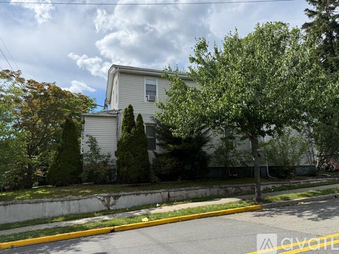A house with a white siding and a grey roof is surrounded by trees and bushes.