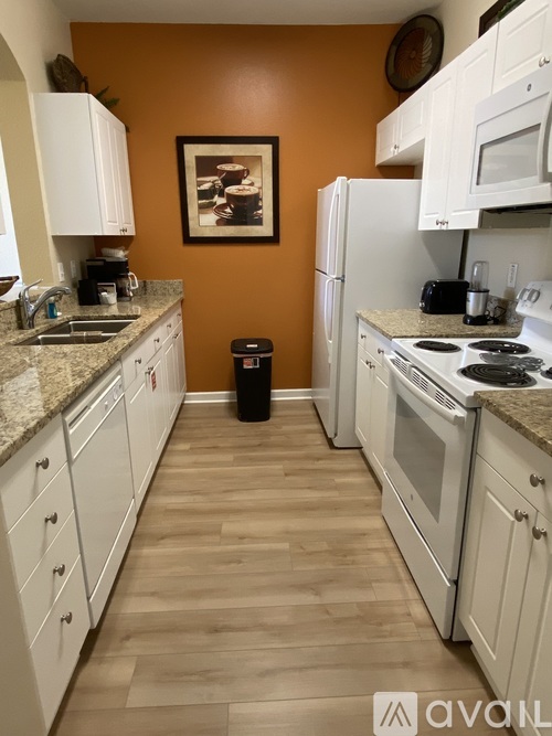 A kitchen with white cabinets and appliances, a fridge, a stove, and a trash can.