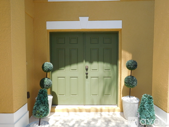 A green door is flanked by two green topiary trees.