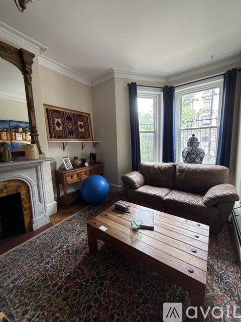 A living room with a brown leather couch, a wooden coffee table, and a fireplace with a mirror above it.