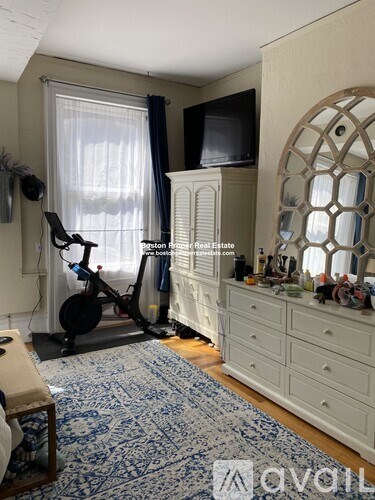 A room with a white dresser, a blue patterned rug, and a window with curtains.
