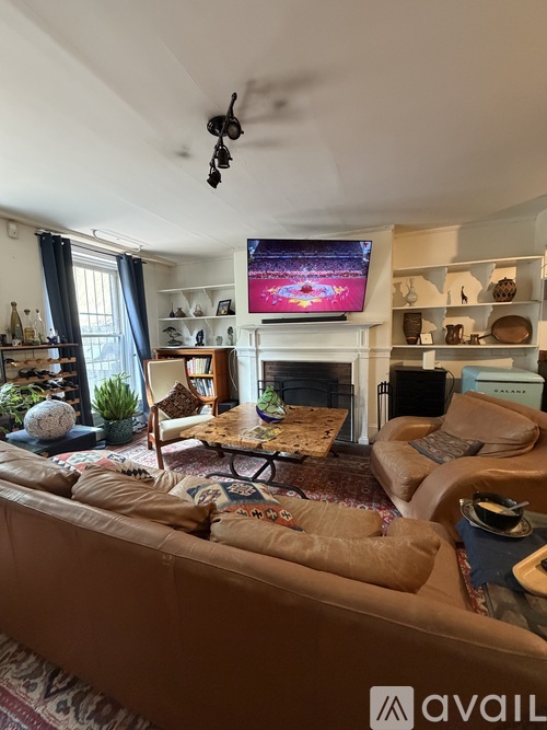 A living room with a brown couch and a television mounted above a fireplace.