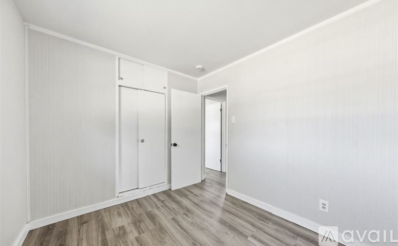 A room with white walls and wooden flooring, featuring a white door and a white wardrobe.