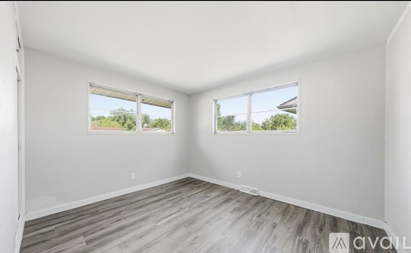 A room with two windows and wooden flooring is available for rent.