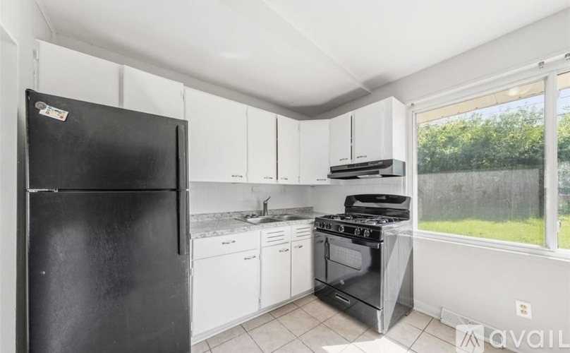A black refrigerator is in a kitchen with white cabinets and a stove.
