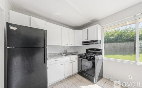 A black refrigerator is in a kitchen with white cabinets and a stove.