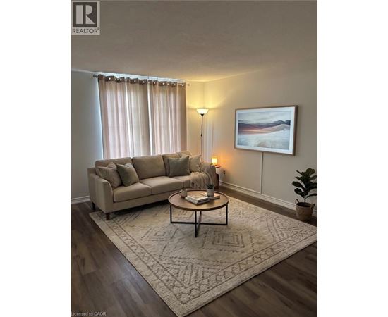 A living room with a beige couch, a coffee table, a lamp, a rug, and a painting on the wall.