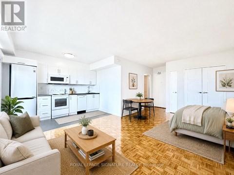 A well-lit, spacious living room with a couch, coffee table, and a bed in the background.