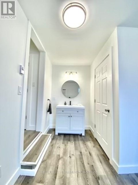 A white bathroom with a round mirror and a wooden floor.