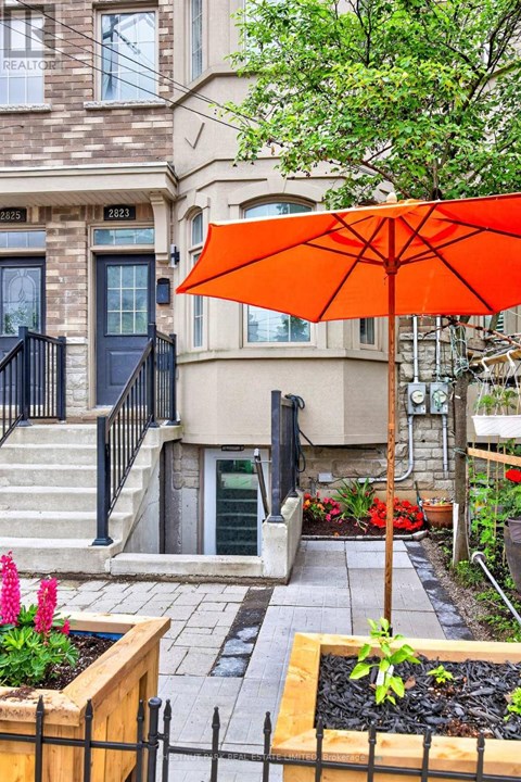 A bright orange umbrella is in front of a building with a black gate.