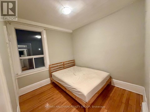 A bedroom with a bed, wooden floors, and a window.