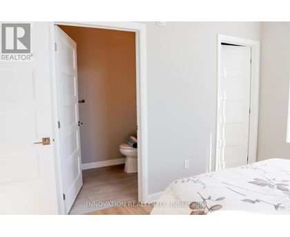 A white door is open to a small bathroom with a toilet and a bedroom with a white bed.