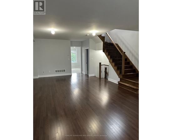 A spacious room with a staircase and wooden flooring.