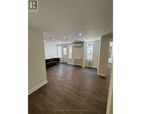 A spacious room with a brown couch and wood flooring.