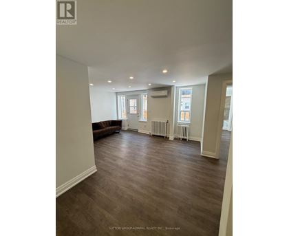 A spacious room with a brown couch and wood flooring.