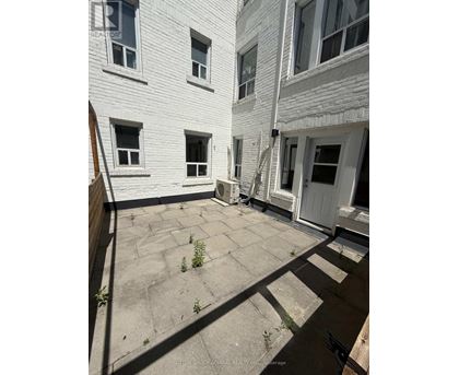 A white building with a grey roof and a small patio with a few plants.