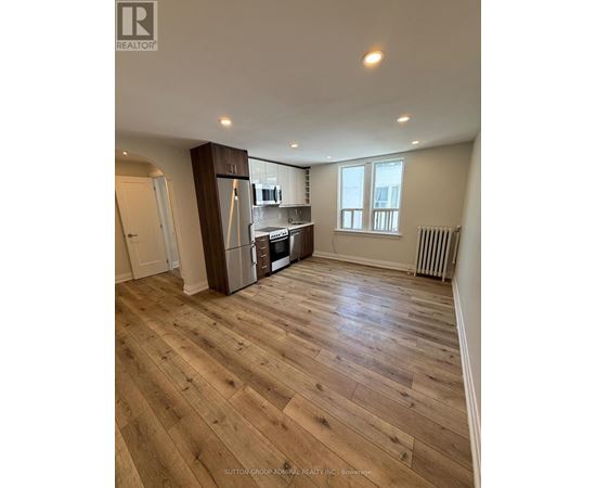 A spacious room with wooden flooring and a kitchen area with stainless steel appliances.