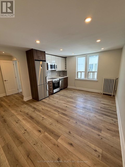 A spacious room with wooden flooring and a kitchen area with stainless steel appliances.