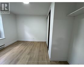 A room with wooden flooring and white walls, with a window on the left side.