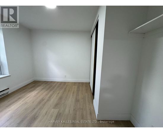 A room with wooden flooring and white walls, with a window on the left side.