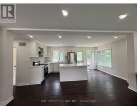 A spacious kitchen and living room with white cabinetry and dark hardwood floors.