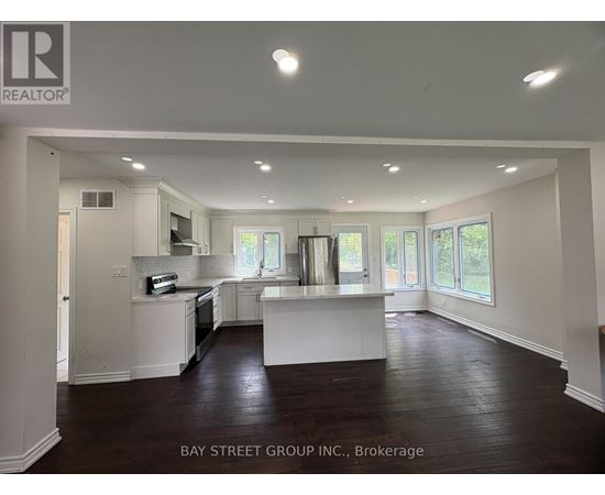 A spacious kitchen and living room with white cabinetry and dark hardwood floors.