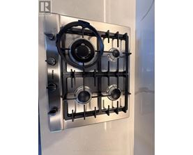 A stainless steel gas stove with four burners and a blue tape around the knobs.