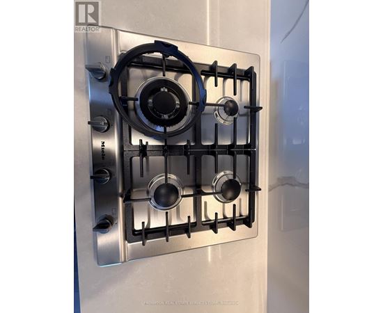 A stainless steel gas stove with four burners and a blue tape around the knobs.