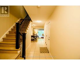 A hallway with a staircase and a dining area in the background.