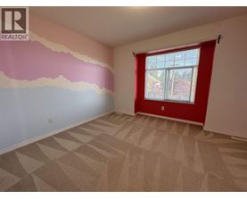 A room with a carpeted floor and a window with a red curtain.