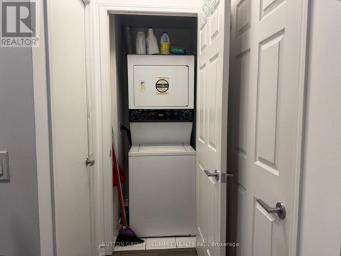 A small white refrigerator is tucked into a narrow space under a door.