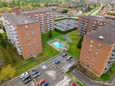 An aerial view of a parking lot between two apartment buildings with cars parked in the lot.