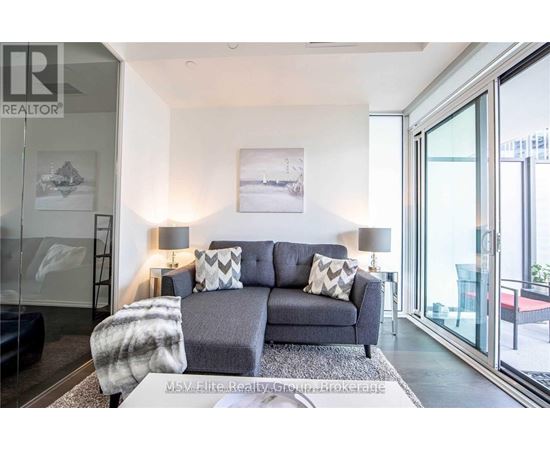 A grey couch with a grey and white blanket on it in a room with a glass door.