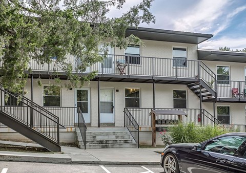 A black car is parked on the street in front of a two-story building with a balcony.