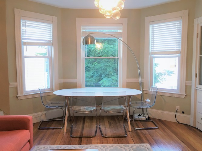 A white table with four chairs is in the middle of a room with a chandelier hanging from the ceiling.