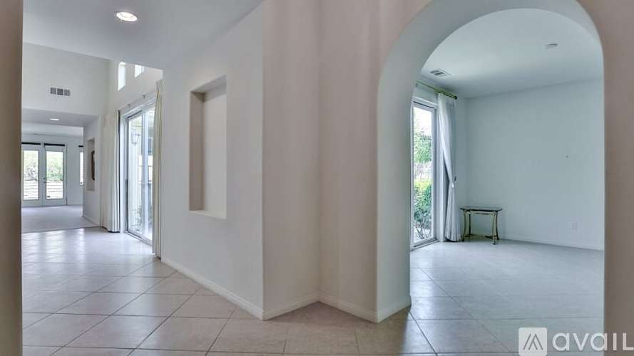 A spacious room with a white floor and walls, and a large archway leading to another room.