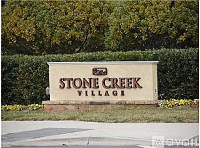 A sign that says Stone Creek Village in front of some trees.
