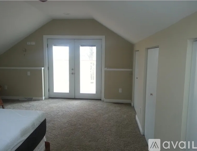 A bedroom with a bed on the left and a window with blinds on the right.