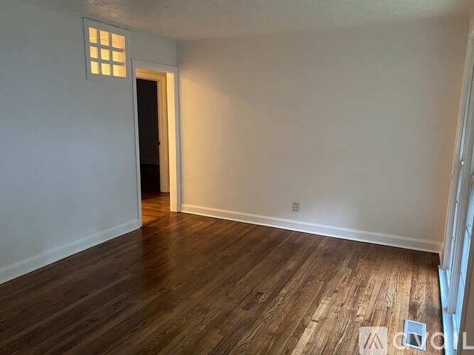 A room with wooden flooring and a window on the left wall.
