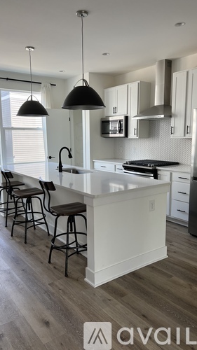 A kitchen with white cabinets and a white island with a black pendant light.