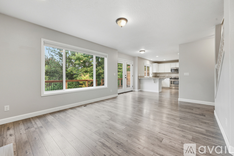 A spacious room with wooden flooring and a large window overlooking a fence.