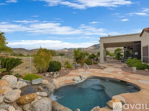 A pool surrounded by rocks and a patio area with a mountain view.