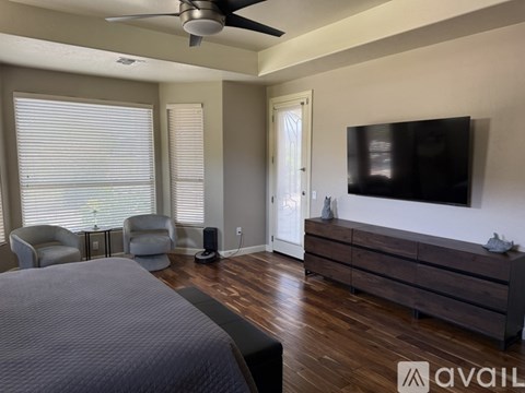 A bedroom with a bed, a chair, a television, and a ceiling fan.
