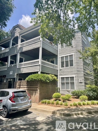 A silver car is parked in front of a grey building with a balcony.