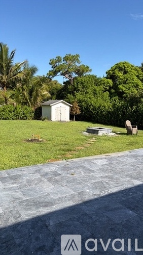 A small white shed sits in a grassy area with a stone pathway leading to it.