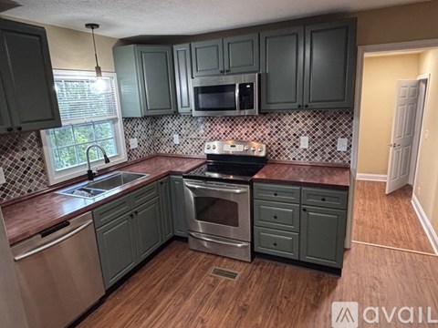 A kitchen with dark green cabinets and a stainless steel dishwasher.