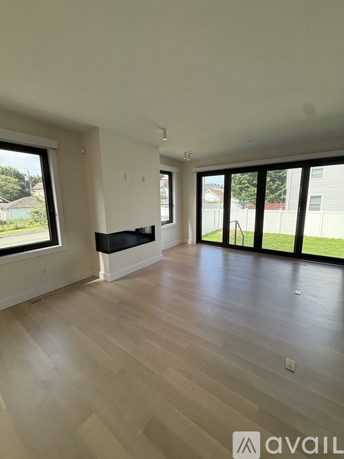 A spacious room with wooden flooring and large windows.