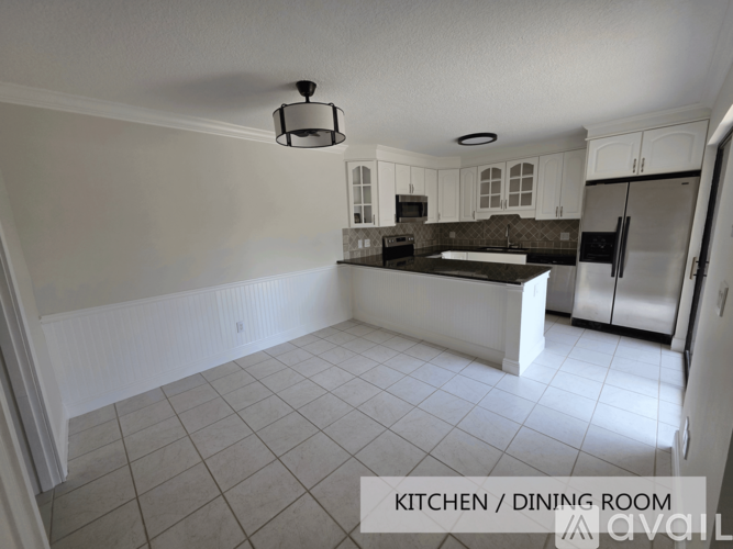 A kitchen and dining room with white cabinets and a black fridge.