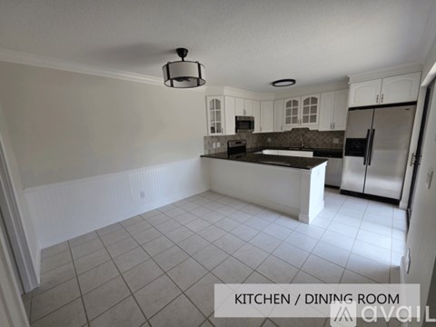 A kitchen and dining room with white cabinets and a black fridge.